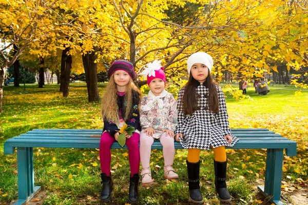 Hösten porträtt av vackra barn på bänken. Glada små flickor med blad i parken i höst. — Stockfoto