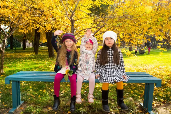 Hösten porträtt av vackra barn på bänken. Glada små flickor med blad i parken i höst. — Stockfoto