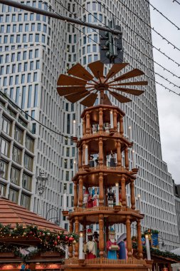 Modern gökdelen ile kentsel arka planda pervane tekerleği olan Noel piramidi. Alman Katolik Yeni Yıl geleneğinde Noel ağacı atlıkarınca