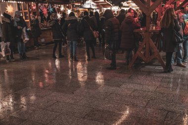 Berlin / Almanya - 12. 24 2019: Kalabalık. Yağmurlu havada Noel pazarında yürüyen bir sürü insan. Islak taşlı zemindeki bulanık yansıma ve arka plandaki bulanık insan figürleri.