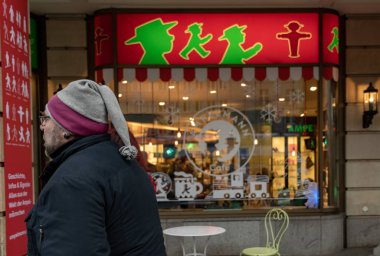 Berlin / Almanya - 12. 24 2019: Berlin 'de Ampelmann sembollü bir hediyelik eşya dükkanı vitrini. Öndeki komik şapkalı yaşlı adam. Arka planda kırmızı ve yeşil dükkan tabelası ve dükkan penceresi.