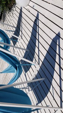 Üçgen şekilli gölgeler, yazları beyaz ahşap döşeme döşemelerine karşı teknelerde yelken açmak gibidir. Güneşli bir günde mavi hamaklı açık deniz mobilyaları. Soyut arkaplan. Işık ve gölgeler. Gölge desenleri. 