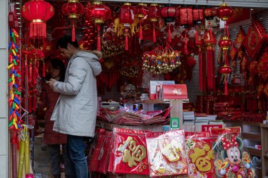 Shanghai / China - 12 05 2019: Man inside oriental souvenir stall at street market with authentic Lunar New Year decorations. Gift shop of traditional Chinese red paper lanterns with red tassels.