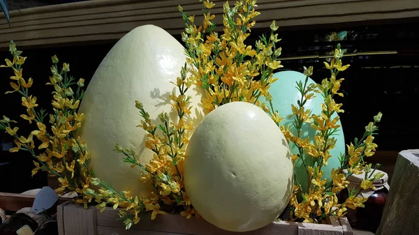 Easter decoration of yellow forsythia branches and three fake eggs of different sizes. Pastel color Easter decorations with copy space. Easter egg decorations. Spring decorative backdrop with copy space. Easter celebration traditions.