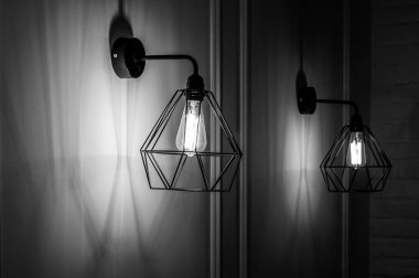 İçinde ampul olan elmas şekilli lamba şeklinde modern kolyenin siyah beyaz fotoğrafı. Minimum tarzda lambalar içinde parıldayan filamanlar. Duvarda şamdanlar asılı. İç aydınlatma.