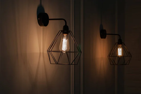 Lamp on a black background. Pendant lights made of diamond shape wire carcass with glass bulb inside. Glowing filament in lamps of minimal style. Sconce lamp hanging on wall. Interior lighting concept.