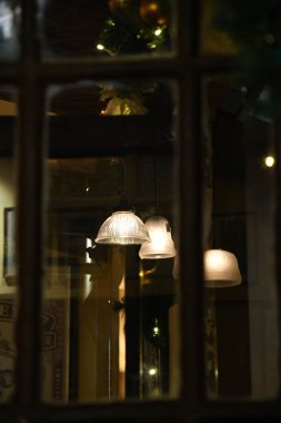 Duvarda lambalar var. Cam penceredeki eski ahşap çerçeveli soyut yansımaların koyu arkaplanı. Altından gece ışıklarıyla parlayan eski abajurların bulanık yansıması..