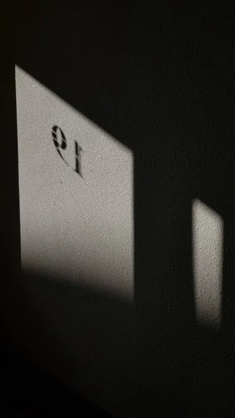 Black and white. Geometric shape shadow of windows on rough cement wall surface. Blurry silhouettes of number 19 symbols on grey textured wall with light and shadow patterns.