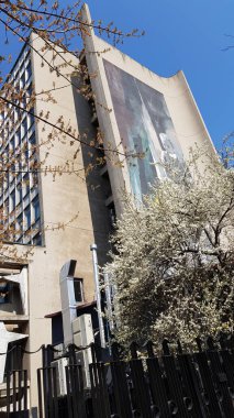 Modern gökdelen cephesinin önündeki kiraz ağaçları berrak mavi gökyüzü arka planına sahipler. İlkbahar mimari şehir manzarası. Güneşli şehir manzarası. Çiçek açan ağaçların dokuları. Bahar mevsiminde park et. Şehir arkaplanı. Mimari altyapılar.