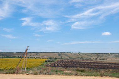Tarımsal tarlalar boyunca köy yolunun yanındaki eski elektrik direği. Kırsal arazi ve açık mavi gökyüzü. Beyaz dönen bulutlar. Avrupa 'da yaz aylarının cennet manzarası.