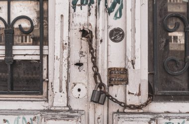 Paslı metal asma kilidin zincirlediği kirli beyaz ahşap kapının mimari detayları. Avrupa şehrinin mimarisi. Dış taraftaki Retro Binası. Evin ön cephesi..