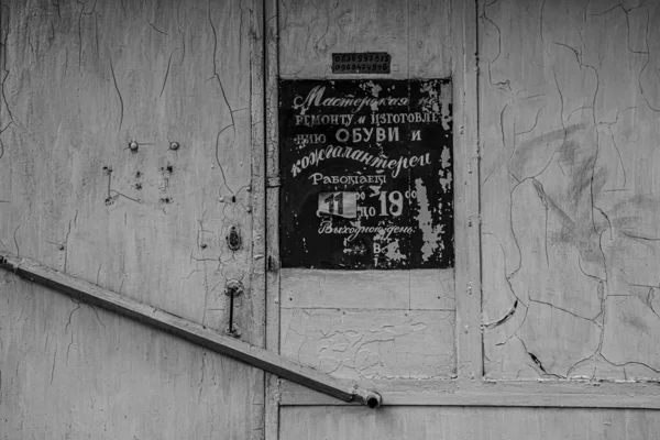 Black and white photo of obsolete signboard with old-fashioned Cyrillic lettering on grunge background of scratched white wall. Details of old building with copy space.