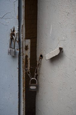 Paslı zincirlerdeki eski asma kilitler gri renge boyanmış eski metal kapılar. Eski metal sapın pürüzlü dokusu ve kapının düzensiz yüzeyi