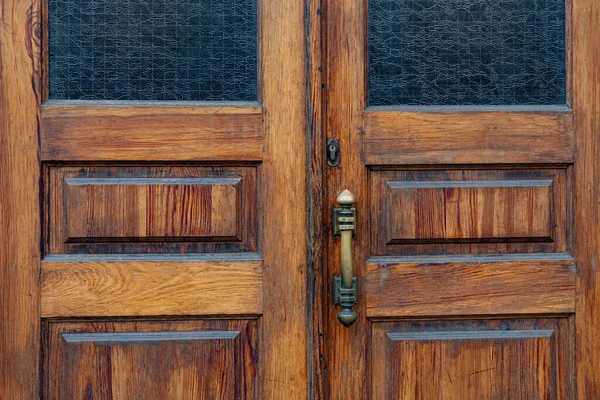 Wooden double door panels with rectangular windows and matte glass inside frames. Retro door knob and keyhole of old lock on grunge wood surface closeup. Building exterior details with copy space