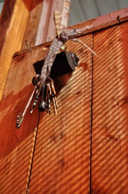 Eski anahtarlar, doğal ahşap kaplamalı kirli örgü örerler. Eski anahtarlar ve güneş ışığında siyah asma kilit. Ahşap zemin üzerinde çizgili gölgeler. Çiftlik evinin penceresinin altındaki antik metal anahtarlar.