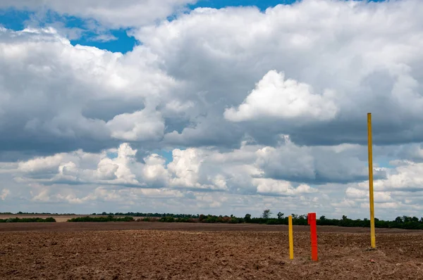 Dramatic sky above rural landscape of brown land field. Metal poles painted in red and yellow colors. Gorgeous cloudscape with white cumulus clouds. rural landscape with plowed field and cloudy sky.