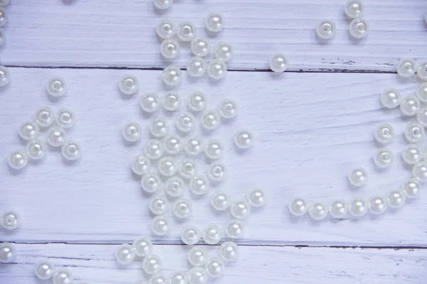 the pearl beads are scattered on a wooden white table.