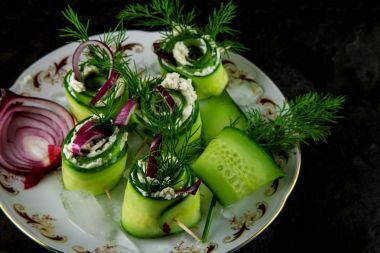 Salatalık ruloları krem peynir, dereotu ve soğan ile dekore edilmiş bir plaka üzerinde