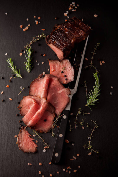 Sliced medium rare grilled roast beef ribeye steak on dark slate kitchen plate background