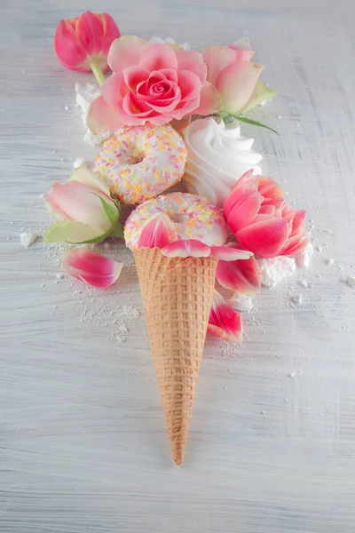 Flatlay waffle sweet ice cream cone with pink tulips and roses blossom flowers over white wood background, top view. Spring or summer mood concept.