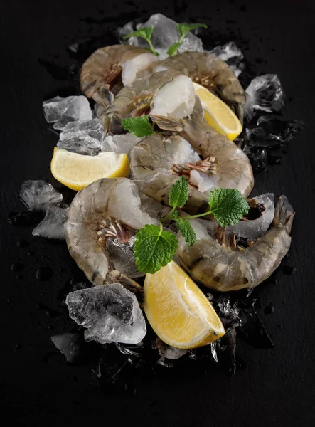 fresh raw king prawns with lemon and lemon balm on dark slate kitchen plate with napkin can be used as background