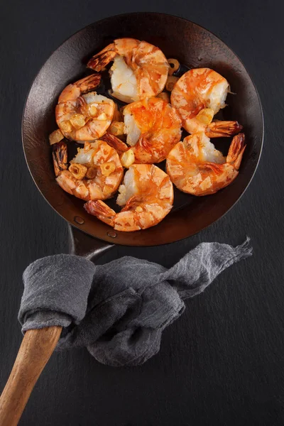 新鲜准备的国王大虾在一个铁平底锅与大蒜在黑暗的石板厨房板材可以作为背景 — 图库照片
