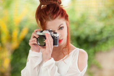 Eski, analog fotoğraf makinesi ile fotoğraf çekmeye bahçesinde oturan Kızıl saçlı güzel genç kadın