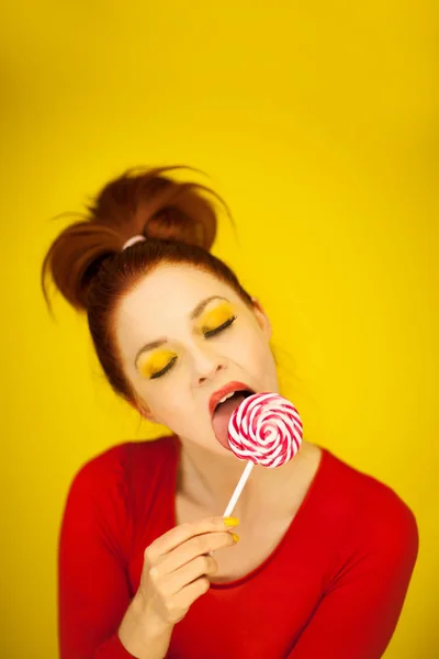 赤と黄色にぴったりの若い魅力的な女性を作る渦のロリポップを保持すること — ストック写真