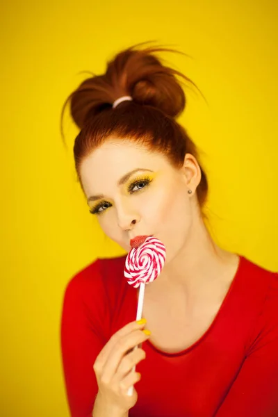 年轻漂亮的女人在红色和黄色与完美的化妆拿着一个漩涡棒糖 — 图库照片
