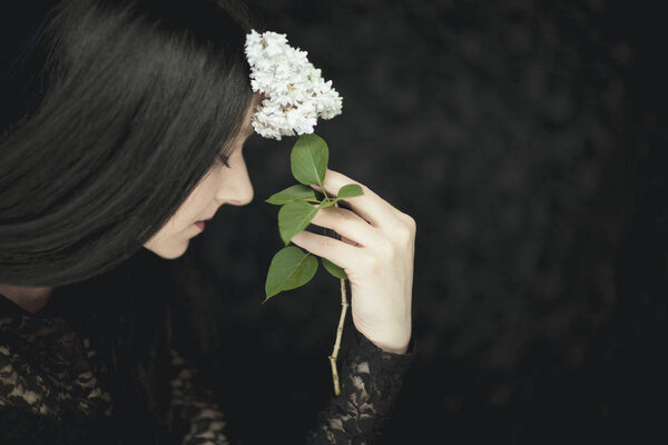 Woman hand holding fresh white lilac flowers to her face, very dark atmospheric sensual rural studio shot can be used as background