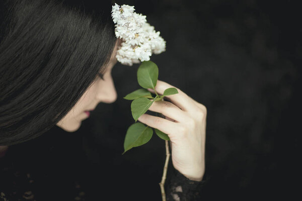 Woman hand holding fresh white lilac flowers to her face, very dark atmospheric sensual rural studio shot can be used as background