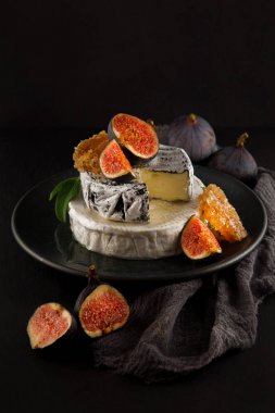 tasty camembert with fresh figs and honey with honeycombs, decorated on a plate on dark background, rustic, moody food photography clipart
