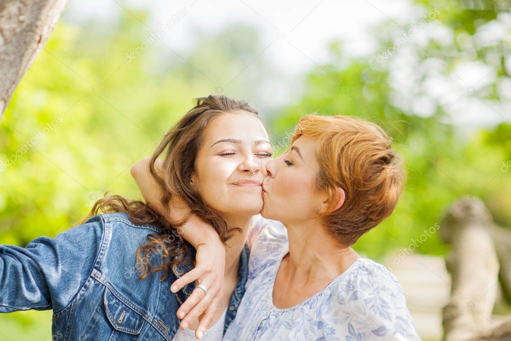 Mother and daughter hug each other, happy and smiling, summer out in the park 