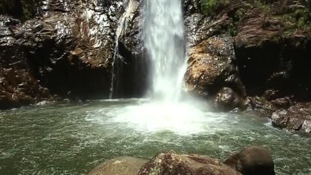 Высокий водопад в пруд с всплесками пены среди скал — стоковое видео