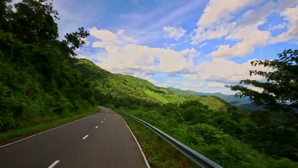 Mouvement vers le bas de la route avec de l'herbe sur le bord de la route parmi le paysage vallonné — Video
