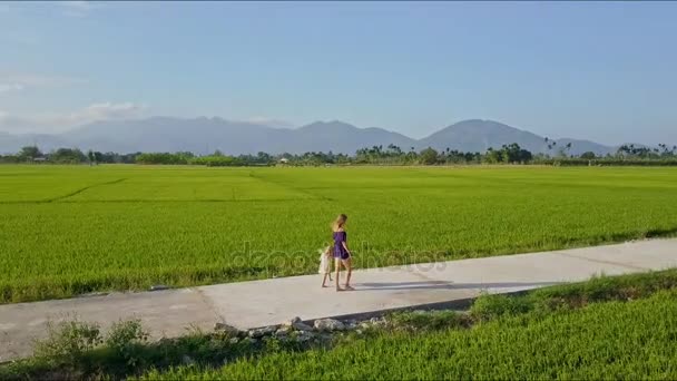 Mujer con hija caminando por el camino entre los campos — Vídeo de stock