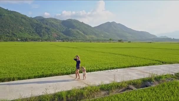 Жінка з дочкою йде по дорозі серед полів — стокове відео