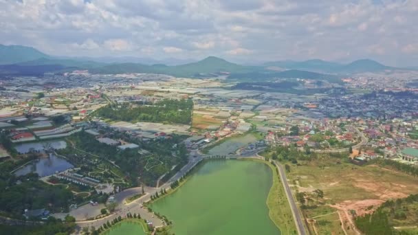 Lac avec bois et pelouses sur les rives contre la ville et les montagnes — Video