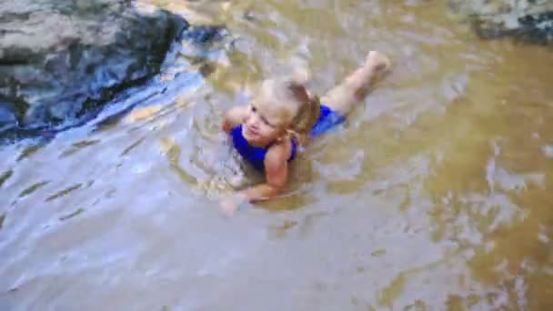 Meisje zwemt in een stroom in de buurt van de waterval tussen rotsen — Stockvideo