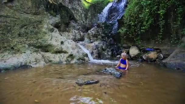 Девушка плавает в ручье возле водопада среди скал — стоковое видео