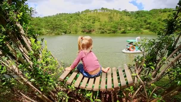 Bambina si siede su una panchina di legno nel parco — Video Stock