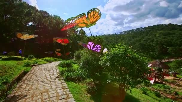 Дорожка среди тропических растений и искусственных бабочек — стоковое видео