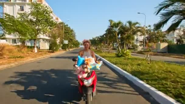 Girl speeds on moped with toys with along road — Stock Video