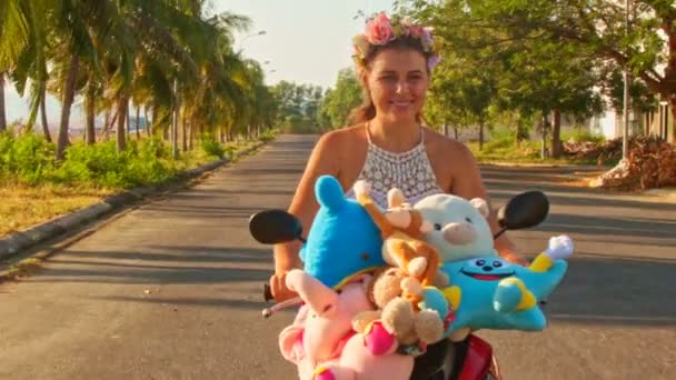 Девушка едет на мопеде с игрушками с вдоль дороги — стоковое видео