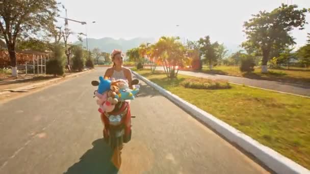 Дівчина прискорюється на мопеді з іграшками вздовж дороги — стокове відео