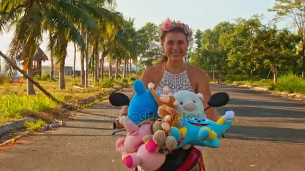 Girl speeds on moped with toys with along road — Stock Video