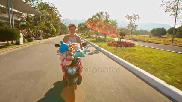 Girl speeds on moped with toys with along road — Stock Video