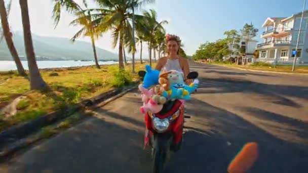 Meisje snelheden op bromfiets met speelgoed met langs de weg — Stockvideo