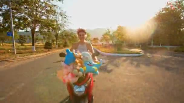 Girl speeds on moped with toys with along road — Stock Video