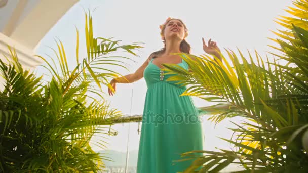 Κοπέλα χορεύει και τραγουδάει ανάμεσα στις παλάμες στο μπαλκόνι — Αρχείο Βίντεο